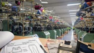 YouSeamless factory demonstrating what is GSM in fabric with a seamless circular knitting machine, tech pack, and material swatches