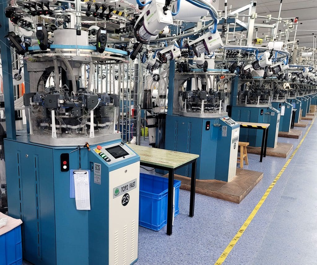 Row of high-precision Santoni TOP2 FAST circular knitting machines in a professional seamless activewear factory for industrial-scale production.