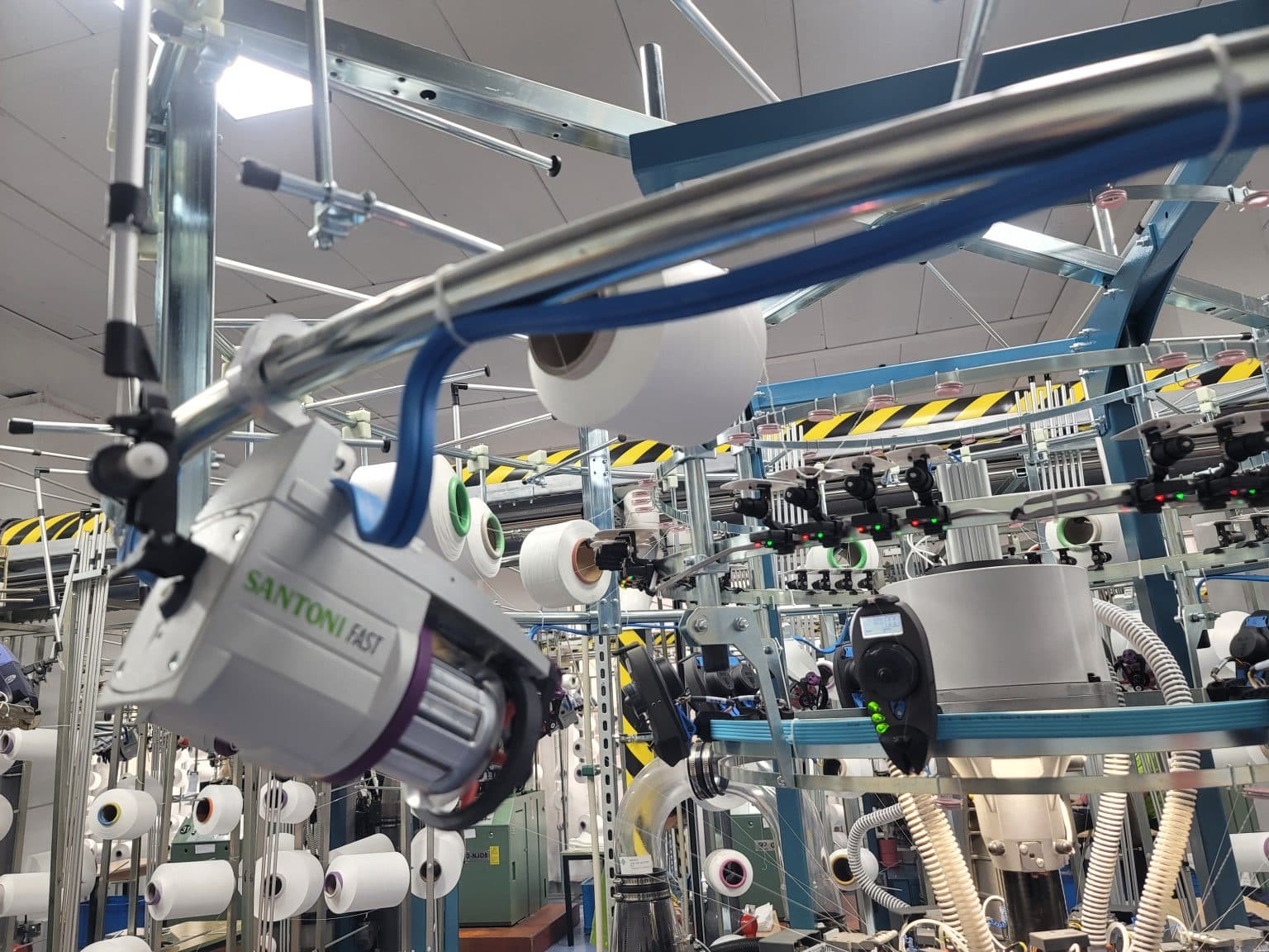 Close-up of a Santoni FAST seamless circular knitting machine with yarn spools in a modern activewear manufacturing factory.