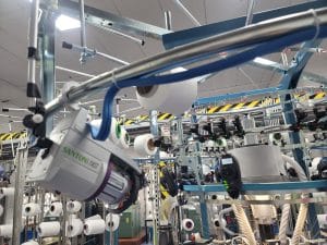 Close-up of a Santoni FAST seamless circular knitting machine with yarn spools in a modern activewear manufacturing factory.